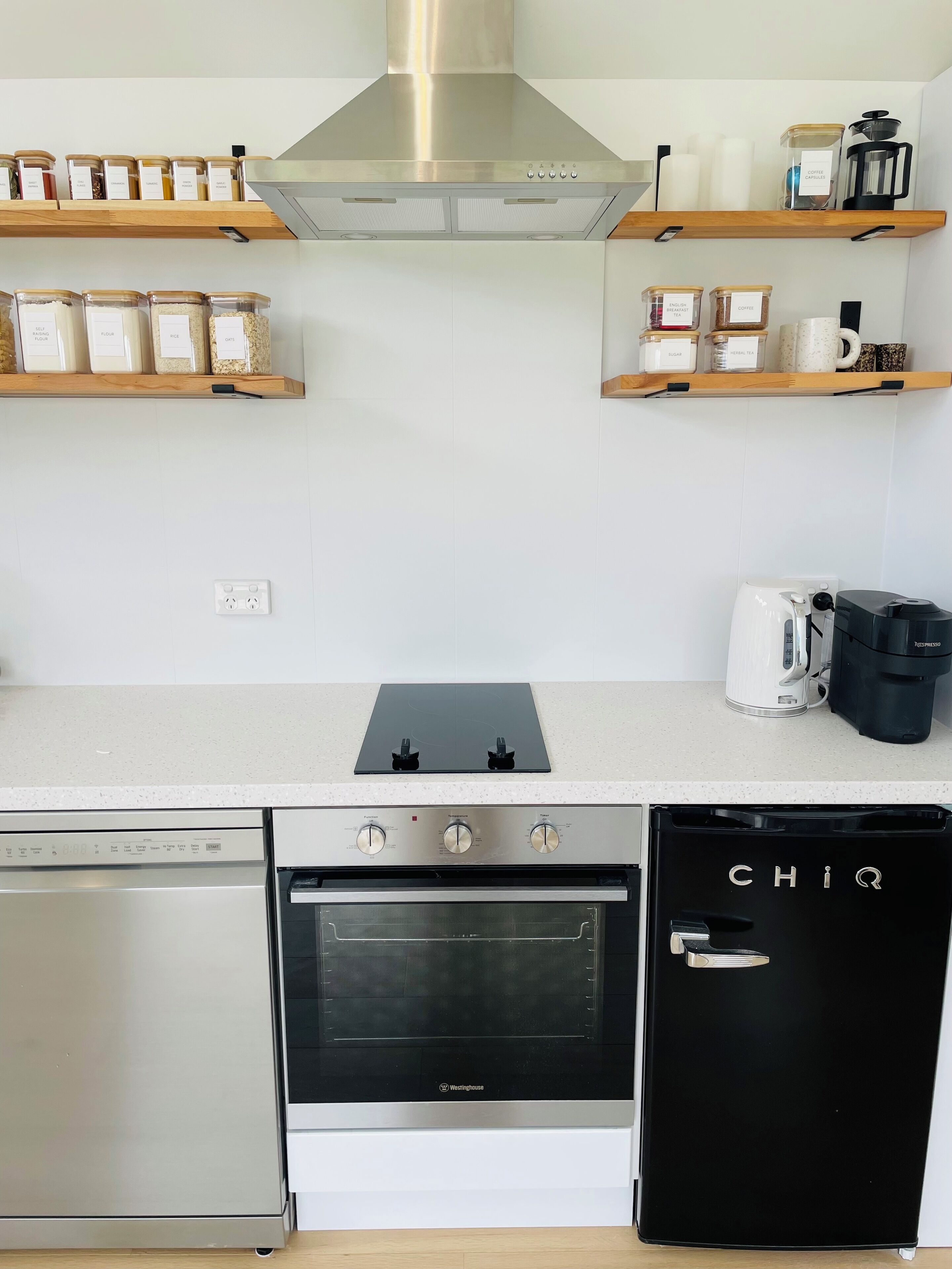 Eine moderne Küche mit Dunstabzugshaube aus Edelstahl, Backofen, Geschirrspüler und Kaffeemaschine.