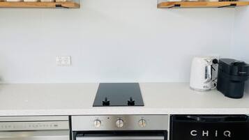 Eine moderne Küche mit Dunstabzugshaube aus Edelstahl, Backofen, Geschirrspüler und Kaffeemaschine.