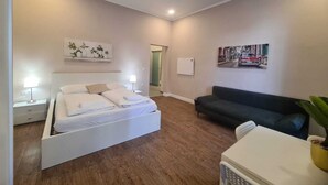 Une chambre moderne avec un lit, des tables de chevet, un canapé et une petite table sur laquelle est posée une plante.