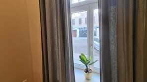 Une vue par une fenêtre, avec des rideaux, une plante en pot et un bâtiment avec des enseignes en arrière-plan.