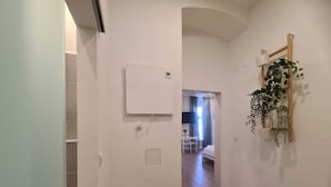 A hallway with a white wall, a mounted air conditioning unit, and a wooden plant shelf. - Smart Stay Near Stadthalle (Vienna)