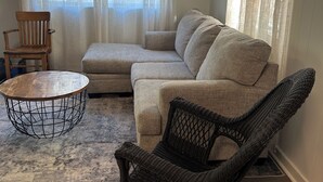 A living room with a sectional sofa, a wicker rocking chair, a round coffee table, and a wooden side table.