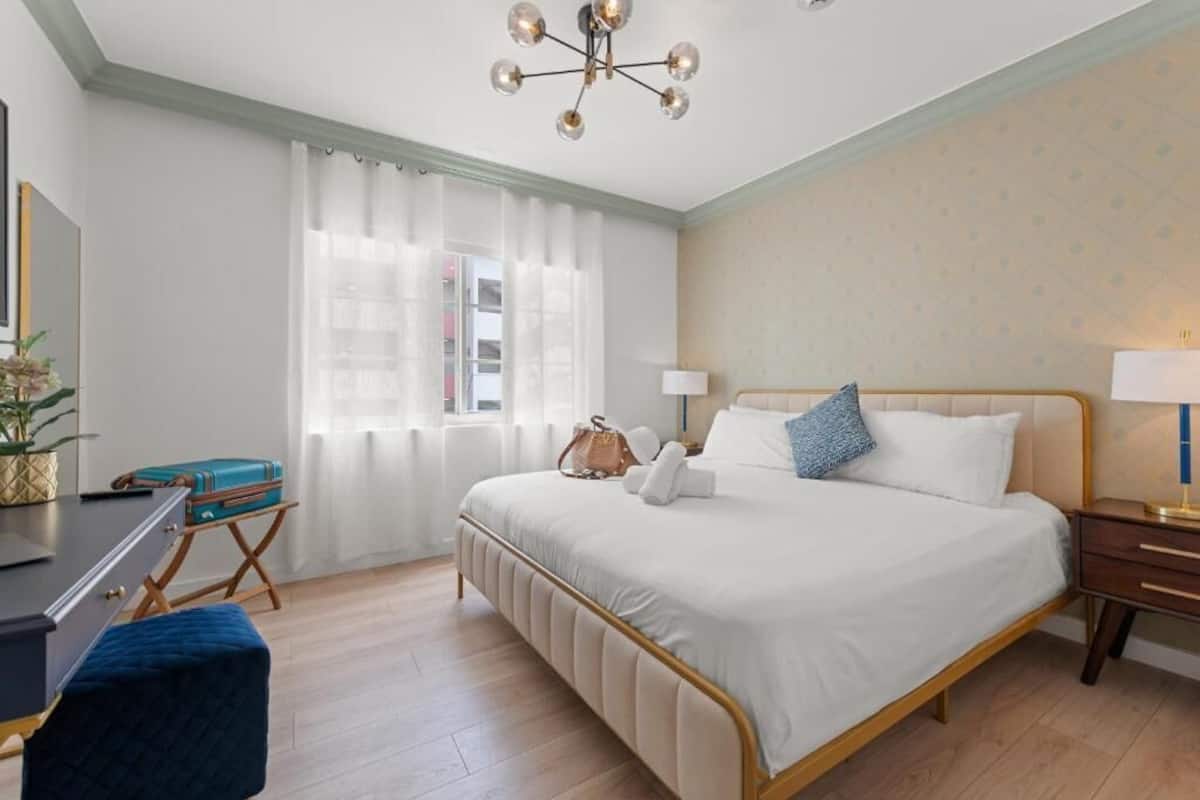 A neatly arranged bedroom with a bed, bedside tables, a desk, and a chair.