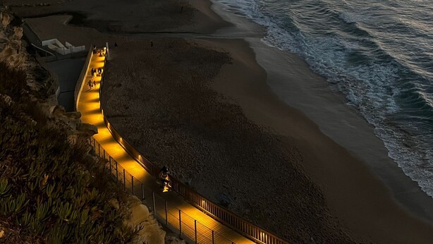 Une promenade en bord de mer, dotée d’une rambarde, qui mène à une plage bordée d’une falaise d’un côt é et de l’océan de l’autre.