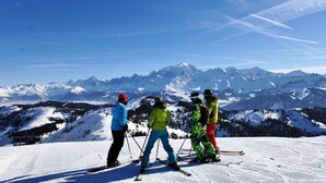 Eine Gruppe von Skifahrern auf einem verschneiten Berghang, im Hintergrund ein freier Blick auf schneebedeckte Gipfel.