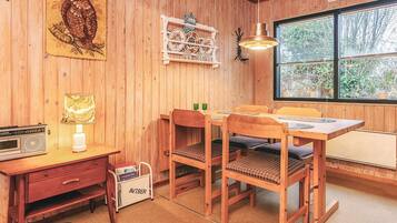 Un interior de madera con una mesa de comedor, sillas, una lámpara, una radio y una estantería.