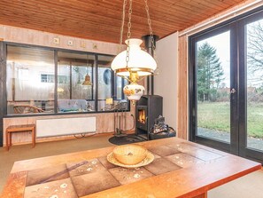 Ein Zimmer mit großem Fenster, einem Tisch mit Korb, einer Hängelampe und einem Kamin.