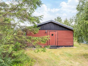 A red wooden building with a black roof, surrounded by greenery and trees. - 4 Person Holiday Home in Hals (Hals)