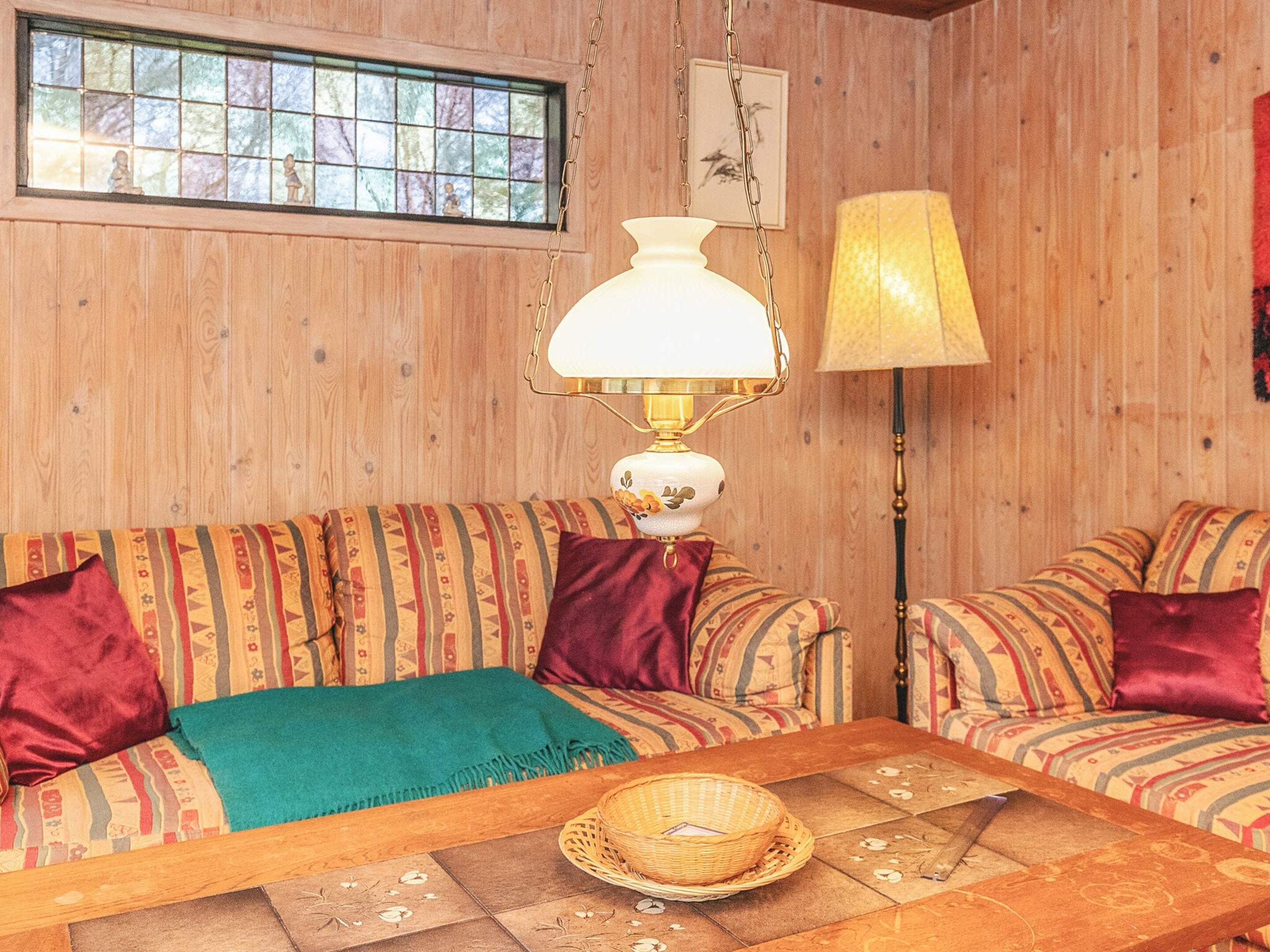 A cozy room with two patterned sofas, a wooden coffee table, a lamp, and a window with a view of trees.