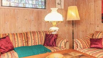 A cozy room with two patterned sofas, a wooden coffee table, a lamp, and a window with a view of trees.