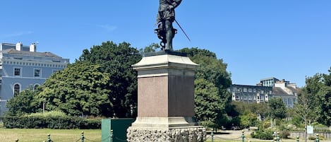 Eine Statue auf einem Sockel in einem Park bei blauem Himmel.