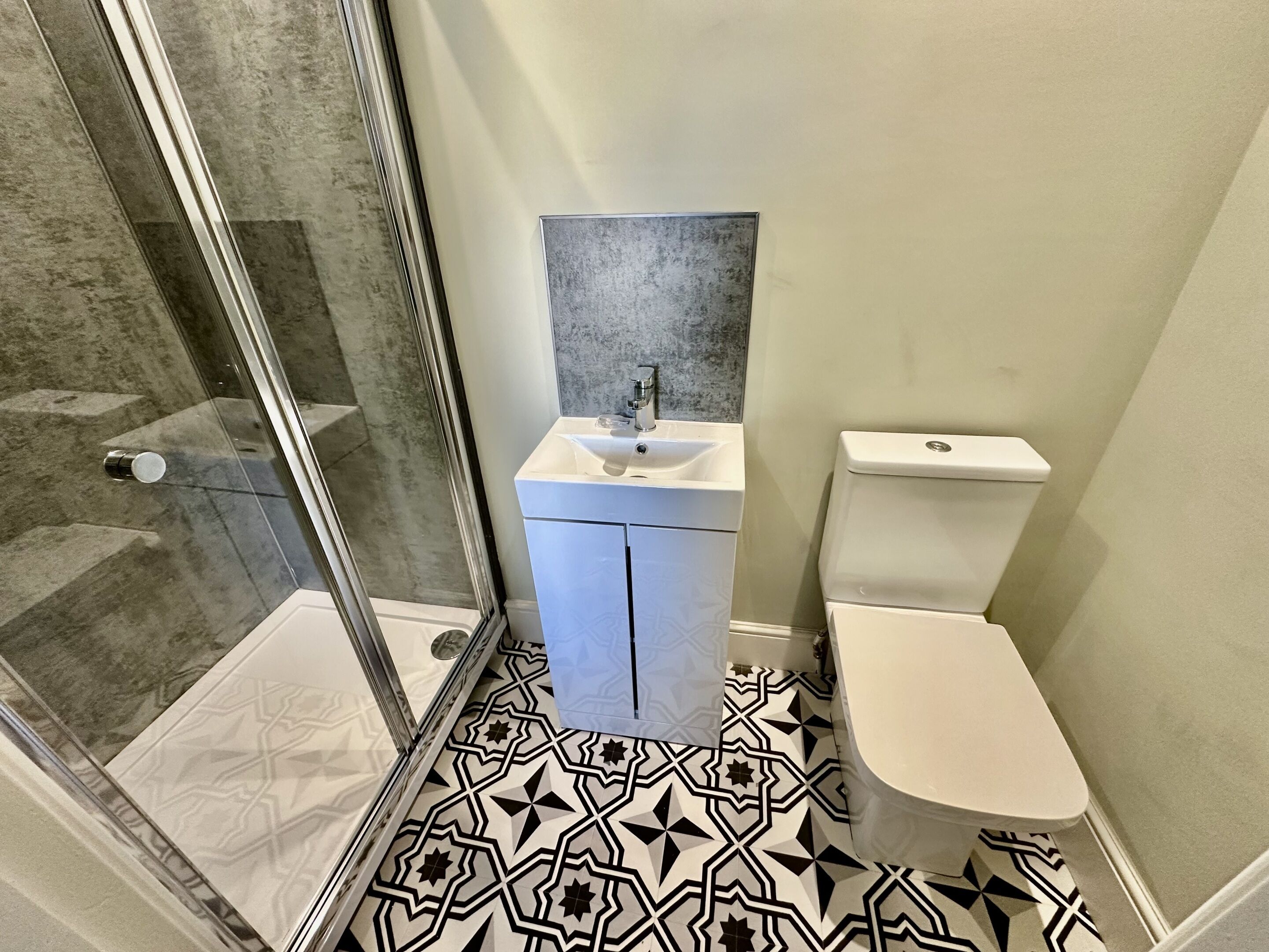 A bathroom with a glass shower enclosure, a white sink with a mirror above it, and a toilet.