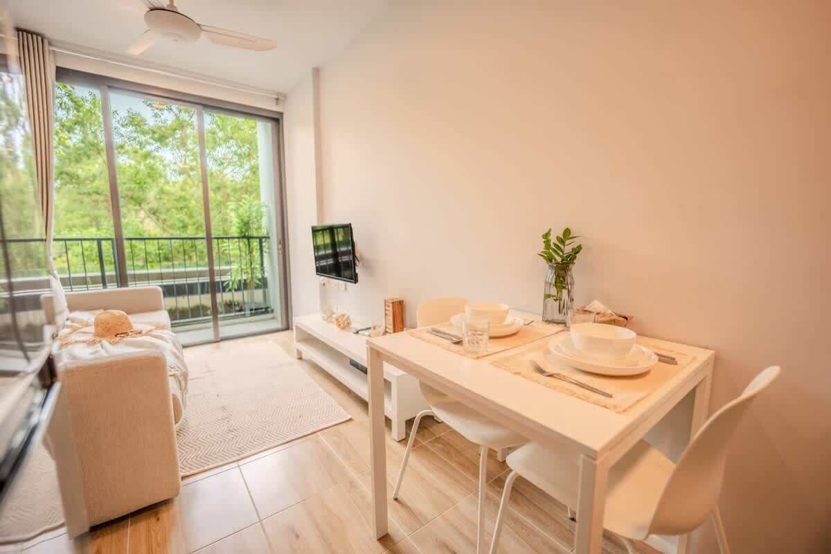 A modern room with a dining table set for two, a sofa, a TV, and a view of greenery outside.