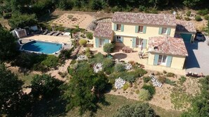 Una casa de dos pisos con piscina, rodeada de árboles y un jardín.