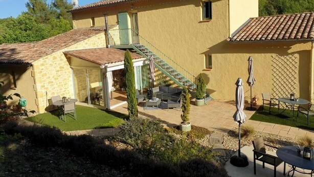 Una casa de dos pisos con un patio, mobiliario exterior y una escalera que conduce al piso superior.