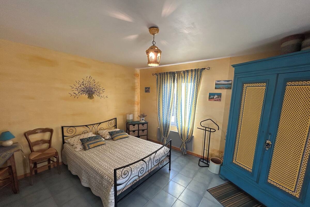 A bedroom with a bed, a chair, a desk, a wardrobe, and a hanging light fixture.