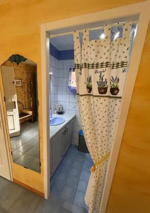 A small bathroom with a white sink, a mirror, and a shower curtain with a floral pattern. - Domaine De JI (Montagnac-Montpezat)