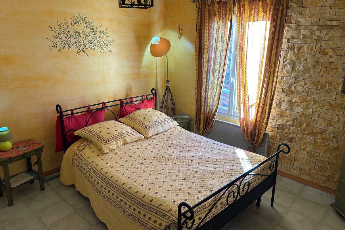 A bedroom with a bed, a nightstand, a lamp, and a window with curtains.