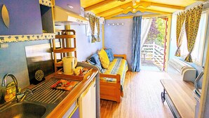 Un ambiente acogedor con un banco de madera, una mesita con un hervidor y una ventana con cortinas.