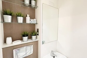A bathroom with a wooden vanity, a mirror, a sink, and shelves with plants and toiletries. - Luxury Classic Studio Kirby Street  (London)