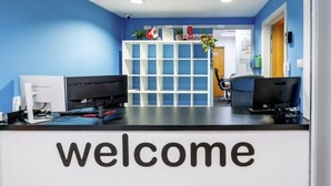 Ein Empfangstresen mit einem 'welcome'-Schild, einem Computer und einer Pflanze.