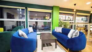 Ein moderner Loungebereich mit blauen Sofas, einem kleinen Tisch und großen Fenstern mit Blick ins Innere und nach außen.