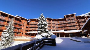 A multi-story hotel with balconies, snow-covered trees, and a clear blue sky. - Apartment in Meribel With Ski-in Access (Les Allues)