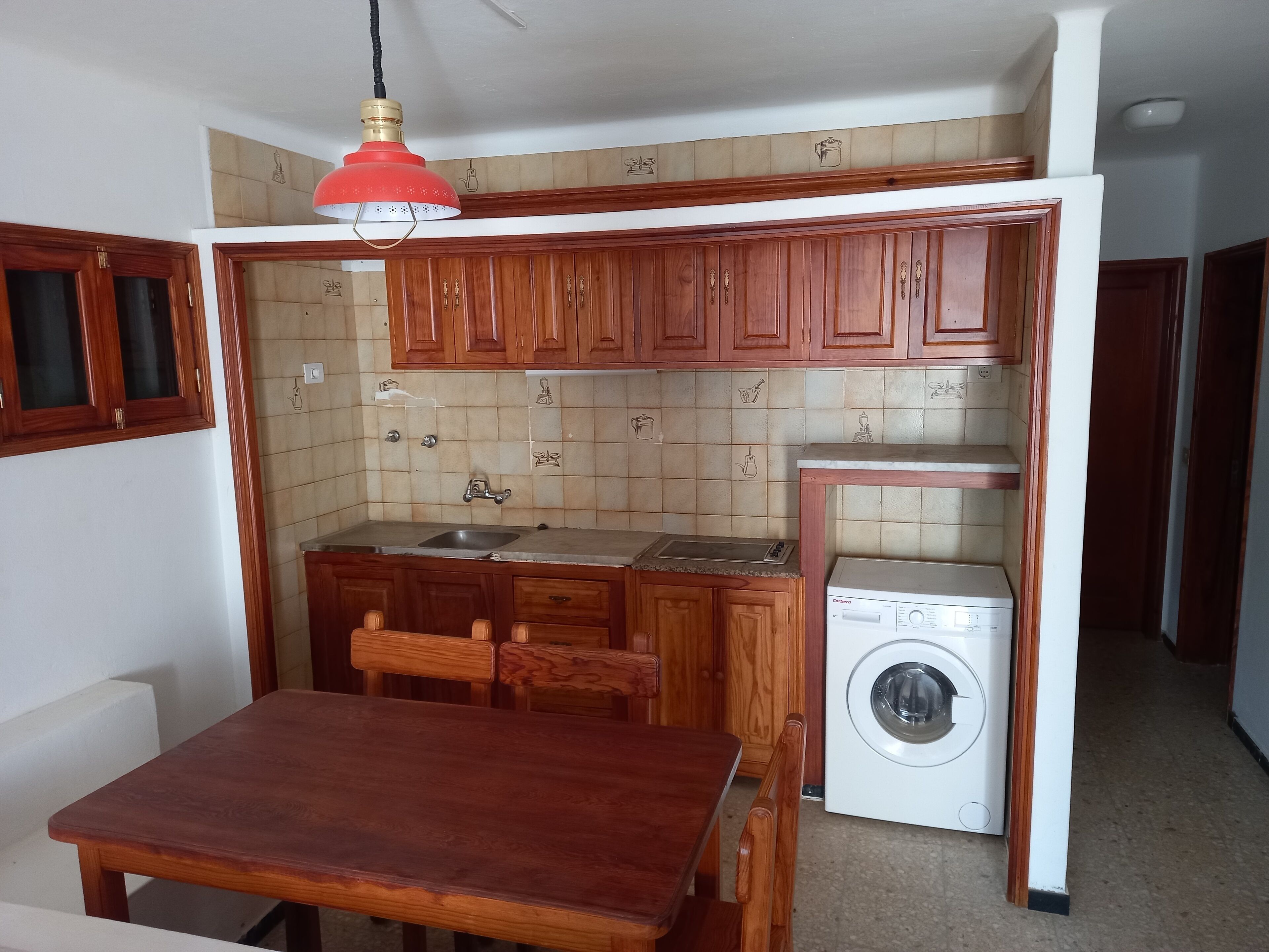 Une cuisine compacte avec des meubles en bois, un évier, un lave-linge et une table à manger avec des chaises.