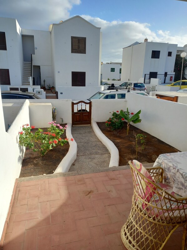 Un patio con edificios blancos, un portón de madera y una silla de mimbre.