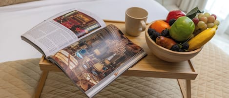 A bed with a quilted cover, a bedside table with a magazine, a bowl of fruit, and a mug.