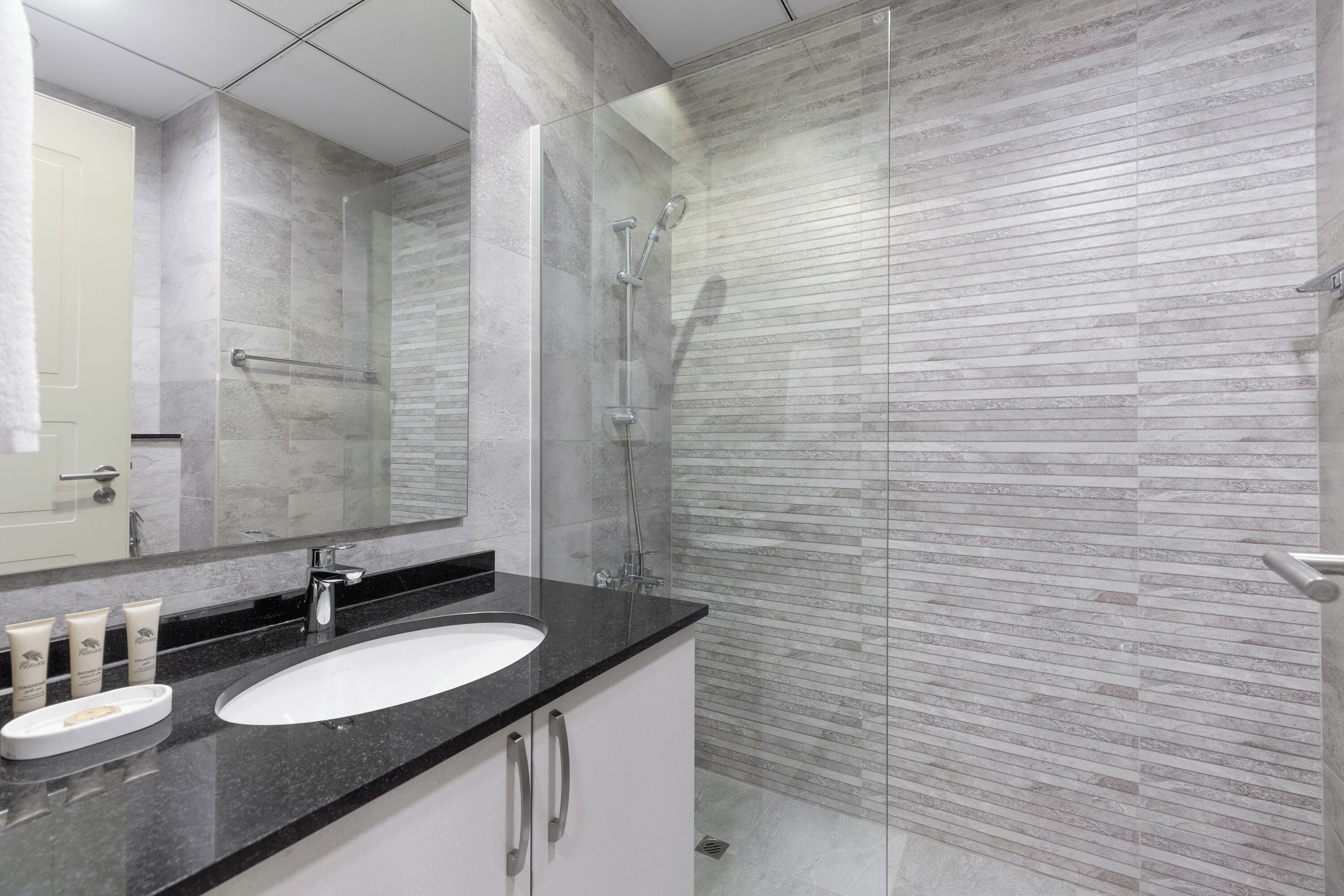 A modern bathroom with a glass-enclosed shower, a white sink, and a large mirror.