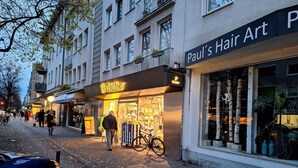 A street view with a building featuring a 'Paul's Hair Art' sign and a 'Tiffany' store. - In the middle of Lindenthal and with the bus right outside the door to the city center (Köln)