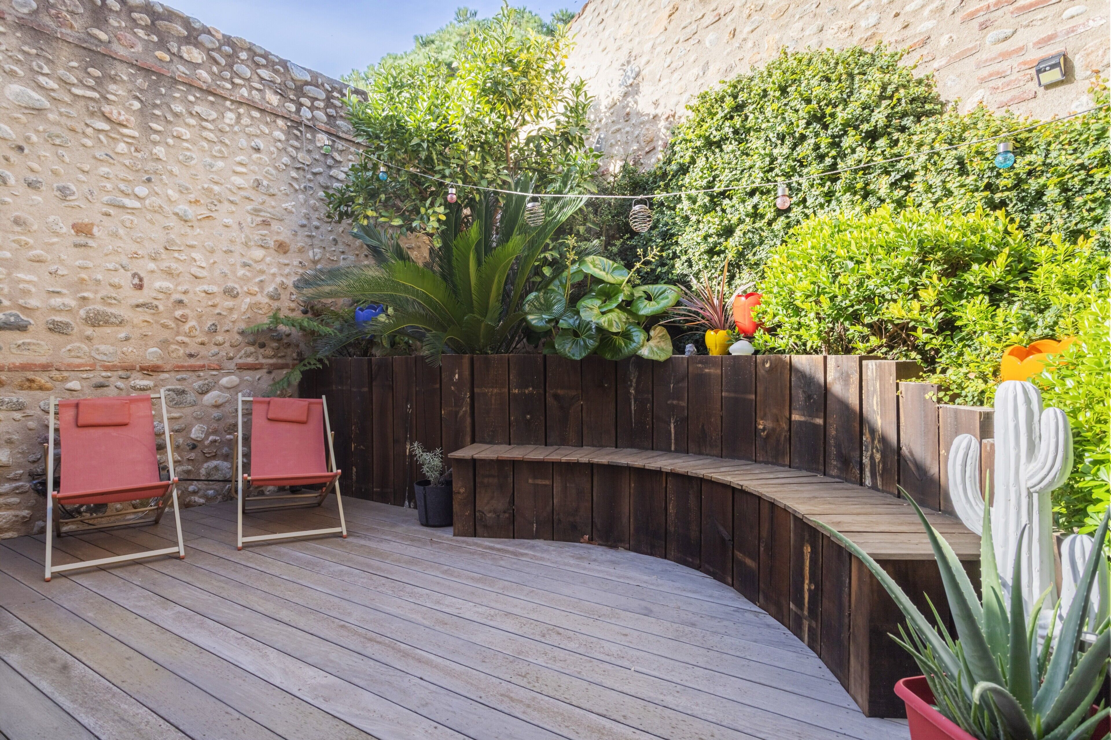 A wooden deck with two red chairs, a curved wooden bench, and a stone wall.