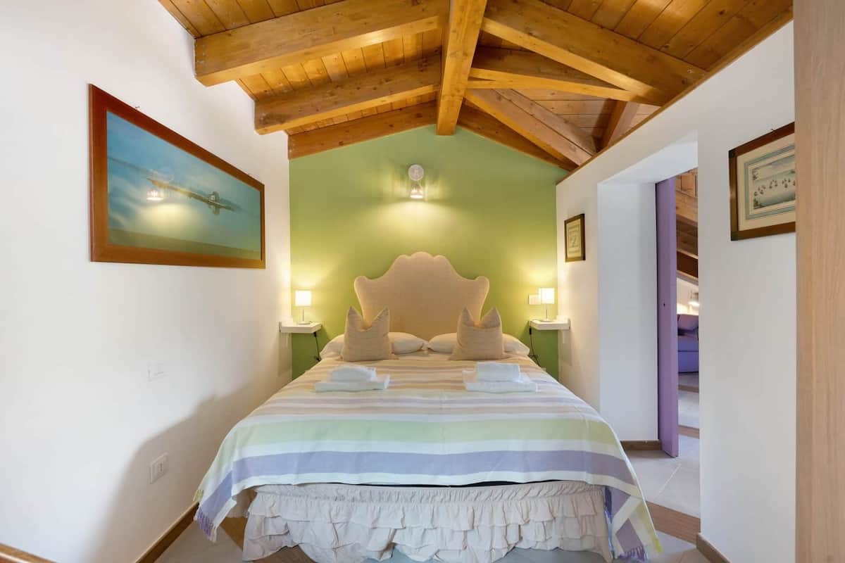 Ein Schlafzimmer mit Holzboden, einem Bett mit gestreifter Bettdecke, zwei Nachttischlampen und einem Gemälde an der Wand.