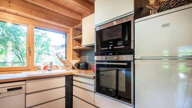 A modern kitchen with stainless steel appliances, wooden cabinets, and a large window providing natural light. - Griotte: Magnificent Chalet in the Center of the Village (Morzine)