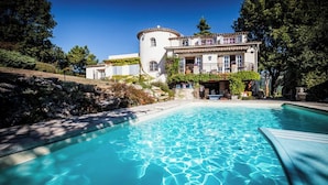 A swimming pool with clear blue water, surrounded by a stone wall and lush greenery. - Beautiful French Riviera Provençal Family Villa with Pool (Châteauneuf-Grasse)