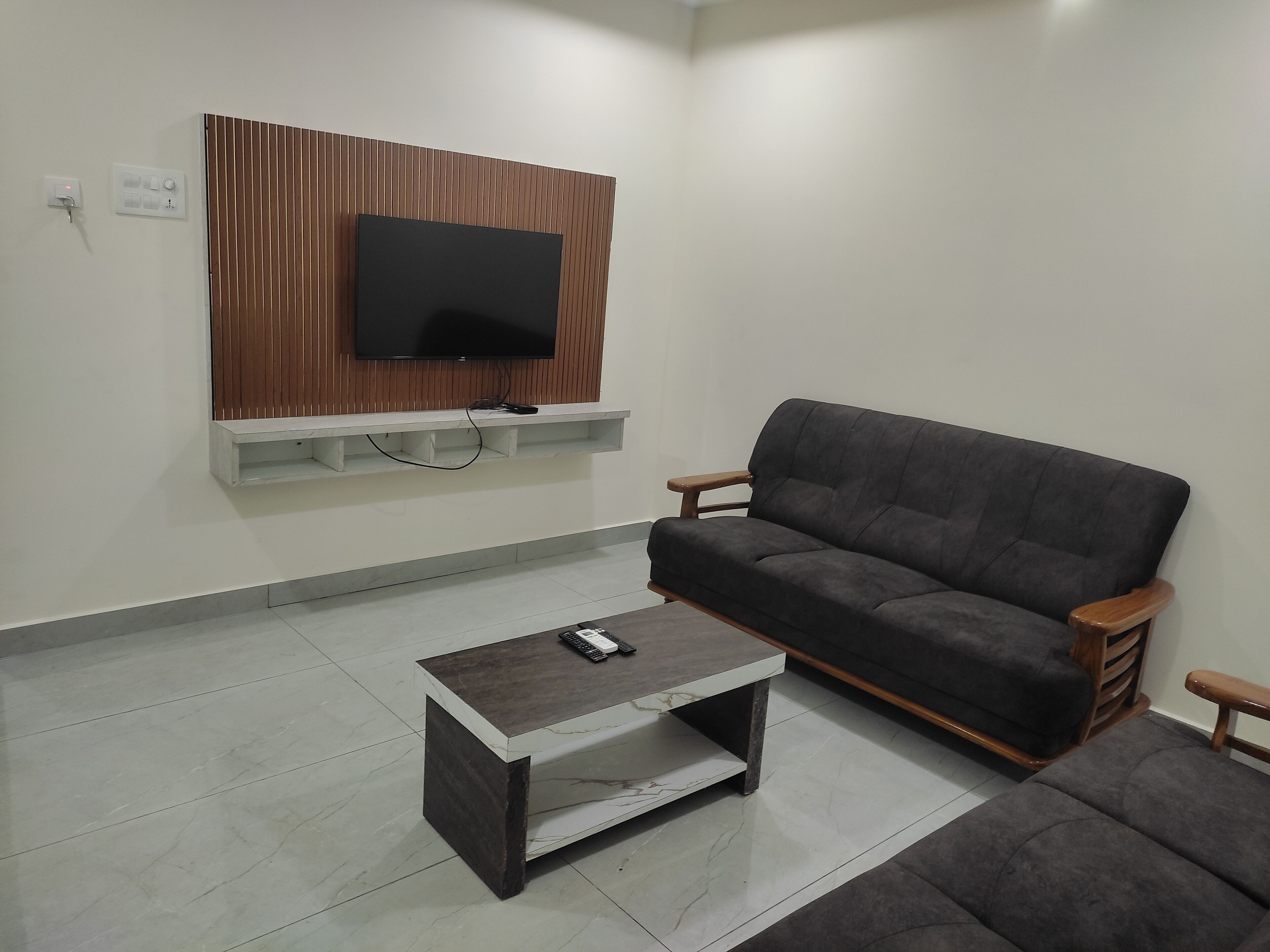 A living room with a sofa, a coffee table, a TV mounted on a wooden panel, and a white shelf.