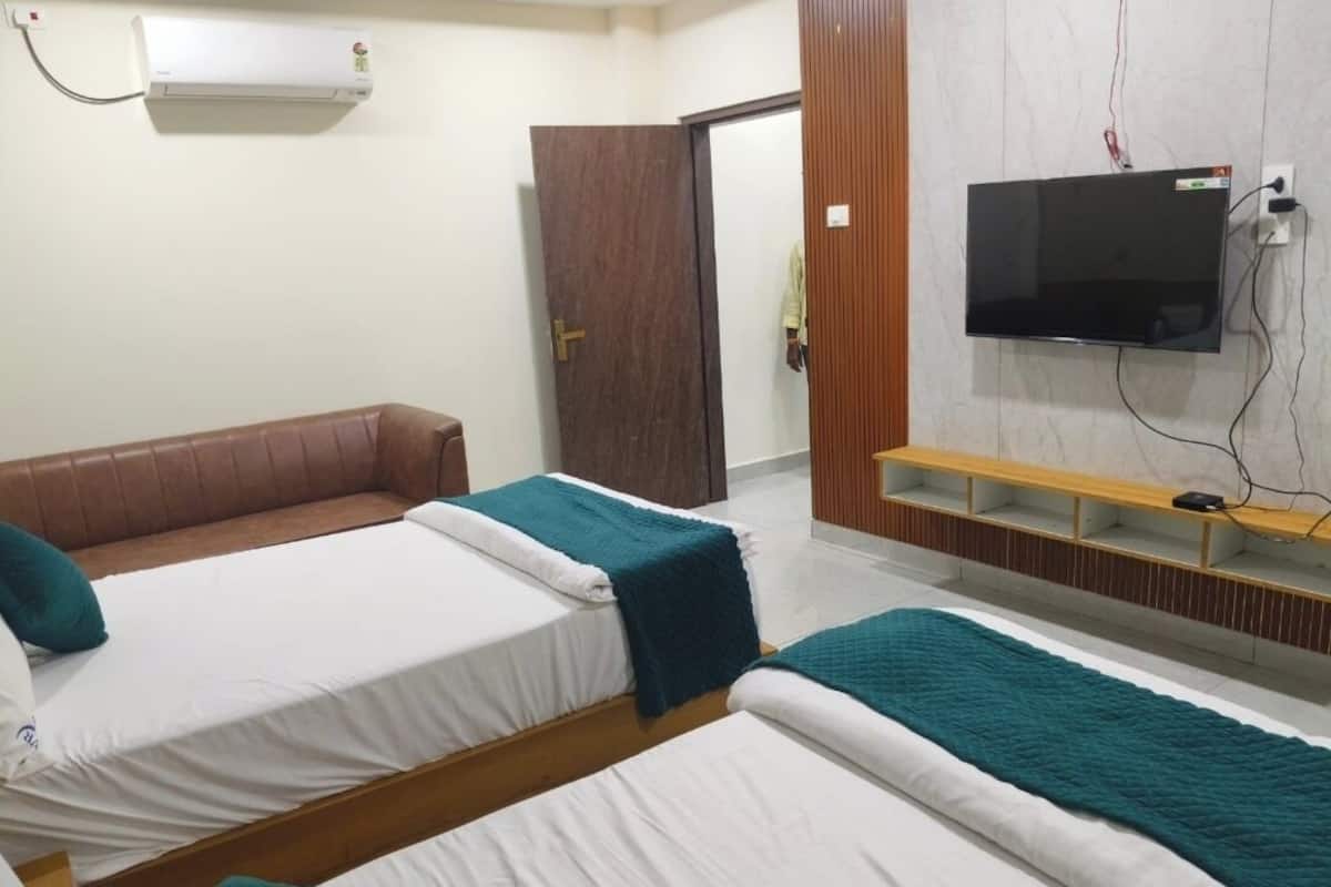 Habitación de hotel con dos camas, un sofá, un televisor y un estante de madera.