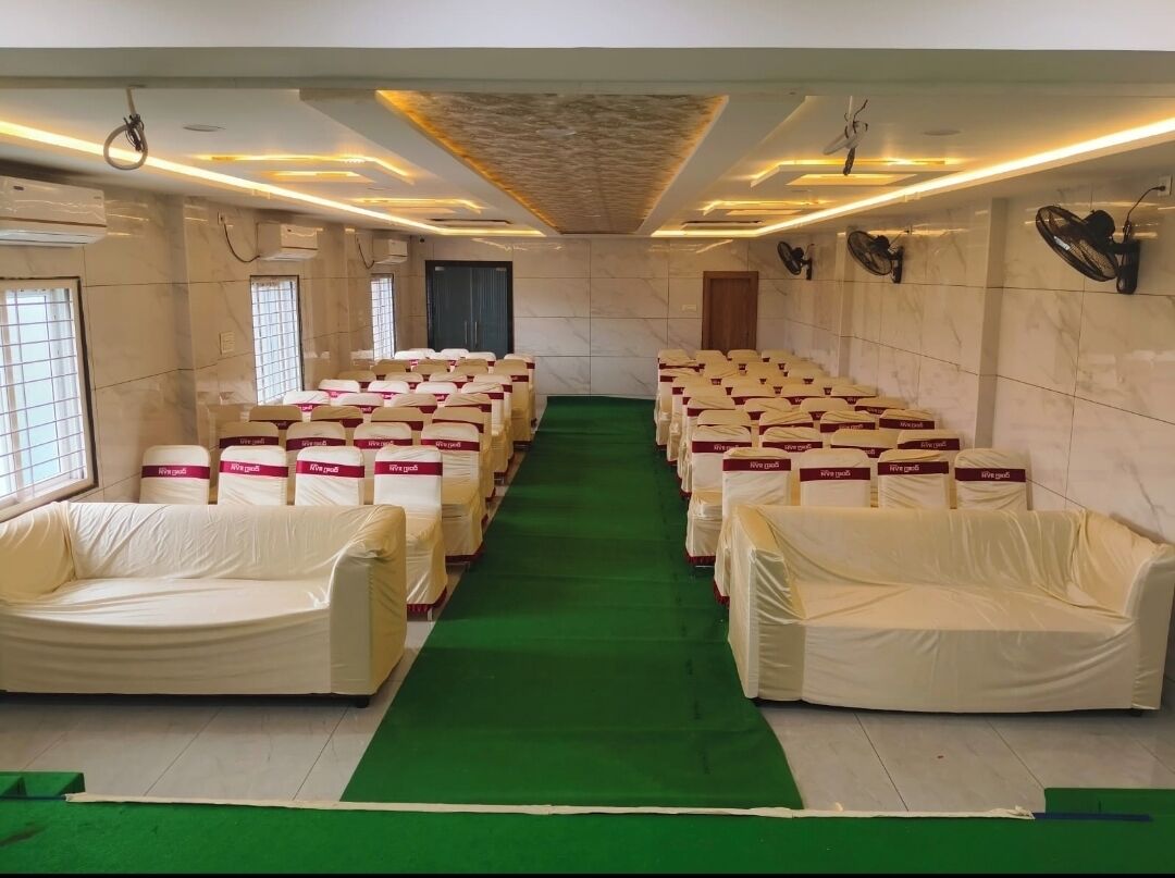 Un salón de conferencias con filas de sillas cubiertas, alfombra verde y ventiladores de techo.