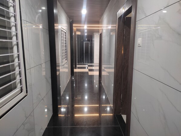 A modern hallway with glossy black and white marble floors, recessed lighting, and a wooden door at the end. - Hotel NVR Grand  (Guntur)