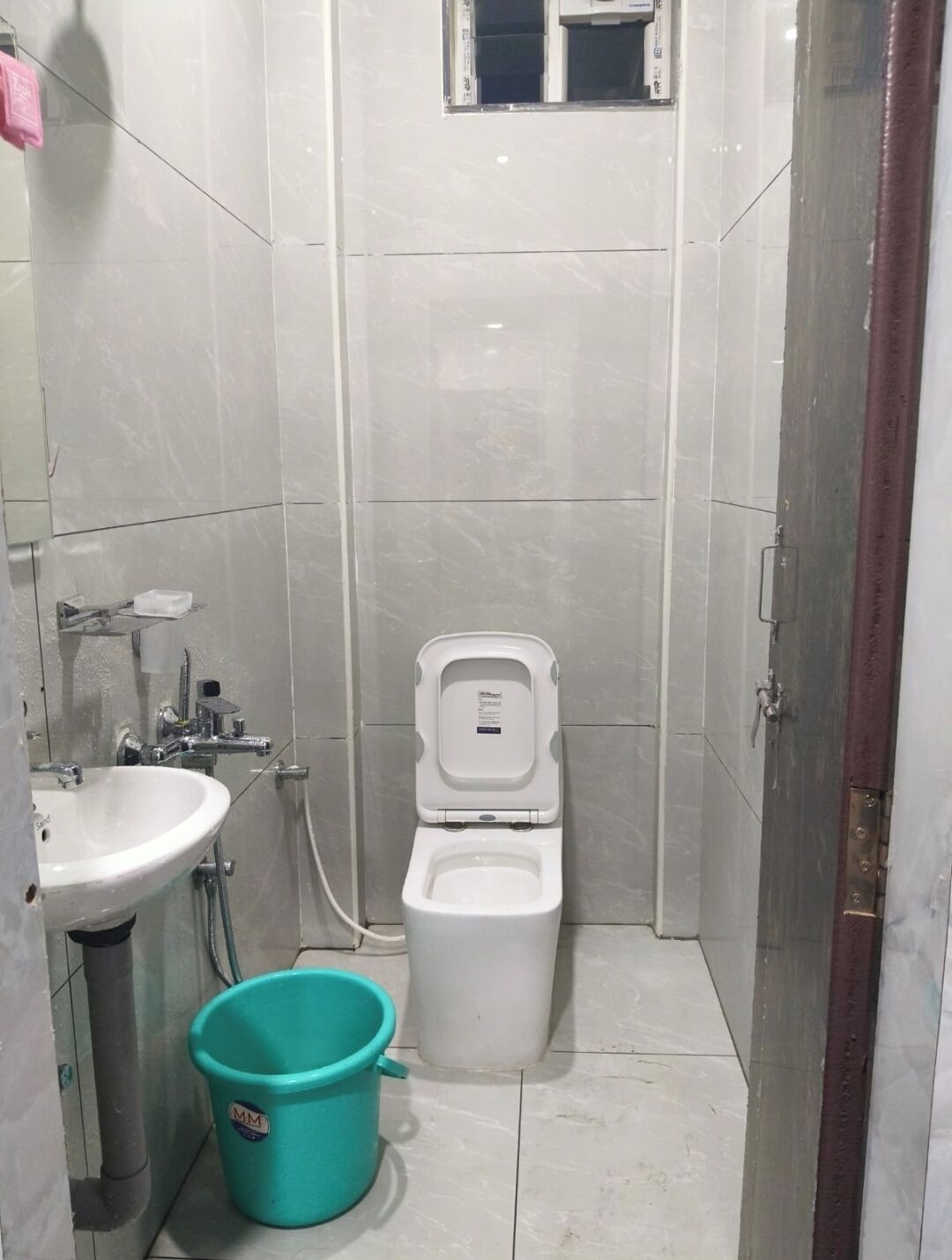 Un baño pequeño con azulejos, un inodoro, un lavamanos y un cubo.