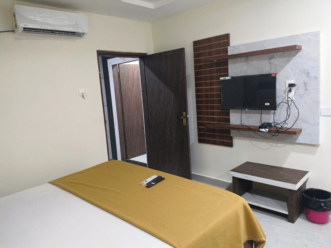 A bedroom with a bed, a TV mounted on the wall, a small table, and a door.