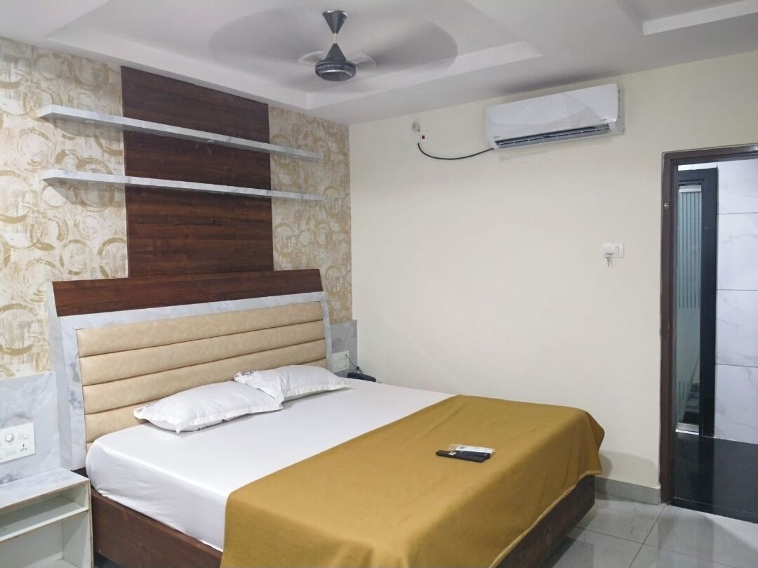 Habitación de hotel con cama, mesita de noche, ventilador de techo y aire acondicionado, además de una puerta.