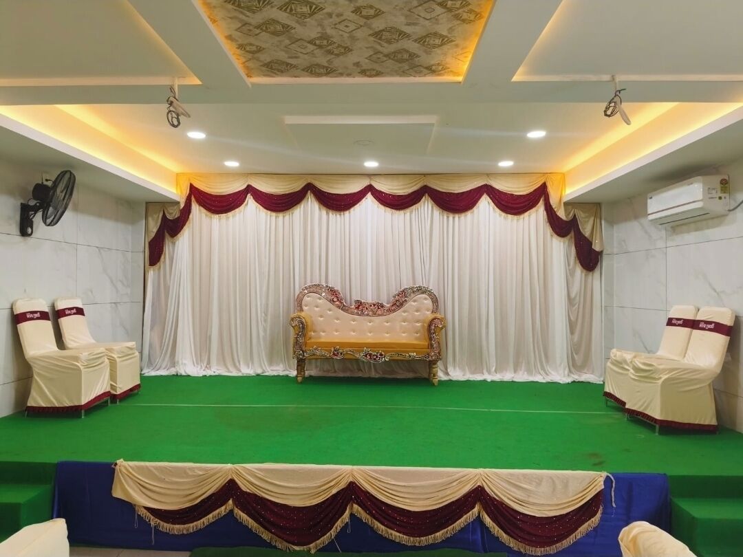 Un escenario con alfombra verde, un sofá y cortinas drapeadas. Hay dos sillas a cada lado del escenario.