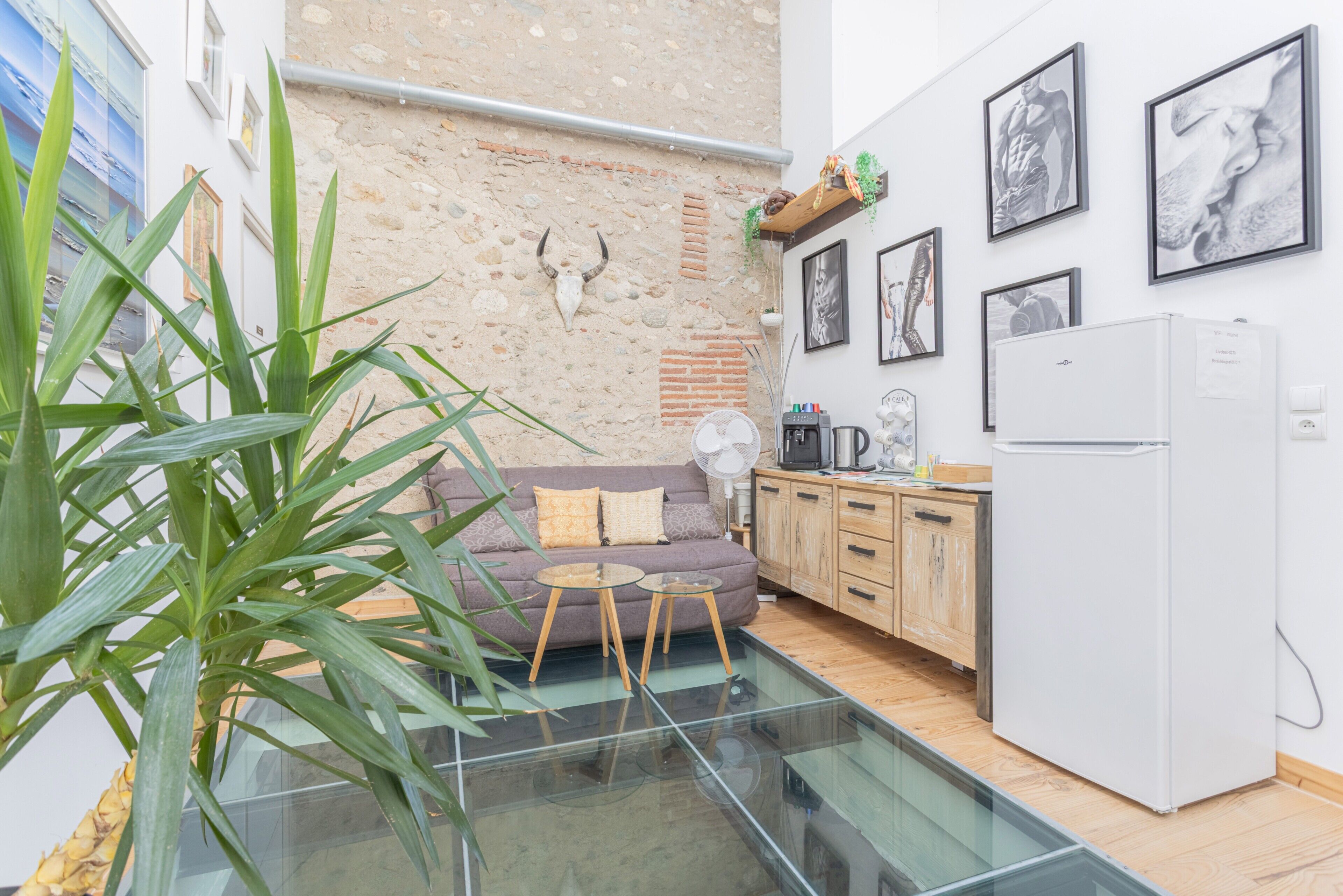 Een moderne woonruimte met een glazen tafel, een bank, een keuken en een stenen muur met een decoratie van een stierenkop.