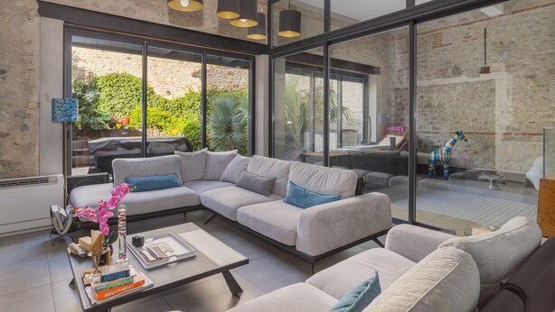 Un salón moderno con un sofá modular, una mesa de centro y una pared de vidrio que ofrece vistas a un jardín y zona de estar al aire libre.