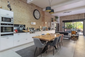 A modern kitchen with a large clock, built-in appliances, and a dining area with chairs and a table. - Namibie Room with Shared Pool and Terrace (Bages)