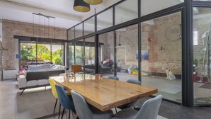 Un interior moderno con una mesa de comedor de madera, sillas grises, un sofá y un separador de vidrio.