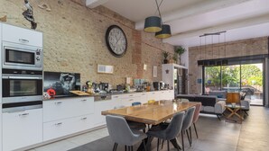 Una cocina moderna con un reloj grande, armarios blancos y un comedor con sillas y una mesa.