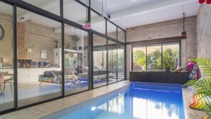 Piscina interior moderna con paredes de vidrio, zona de cocina y vistas al exterior.